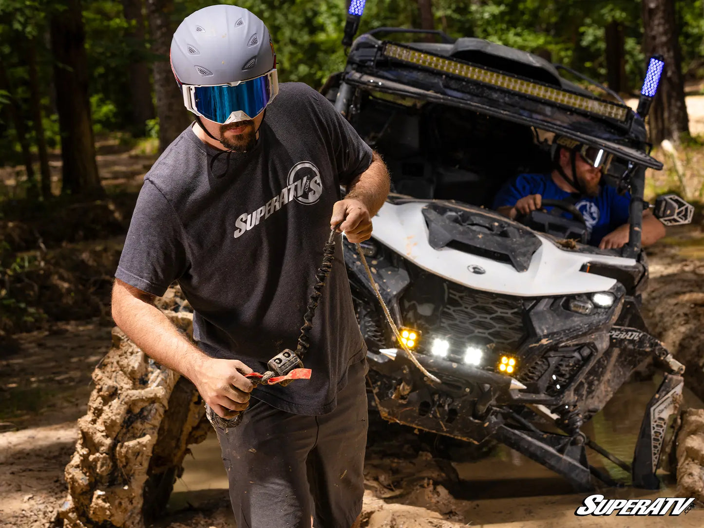 Person with SuperATV gear standing next to an off-road vehicle in a forest setting