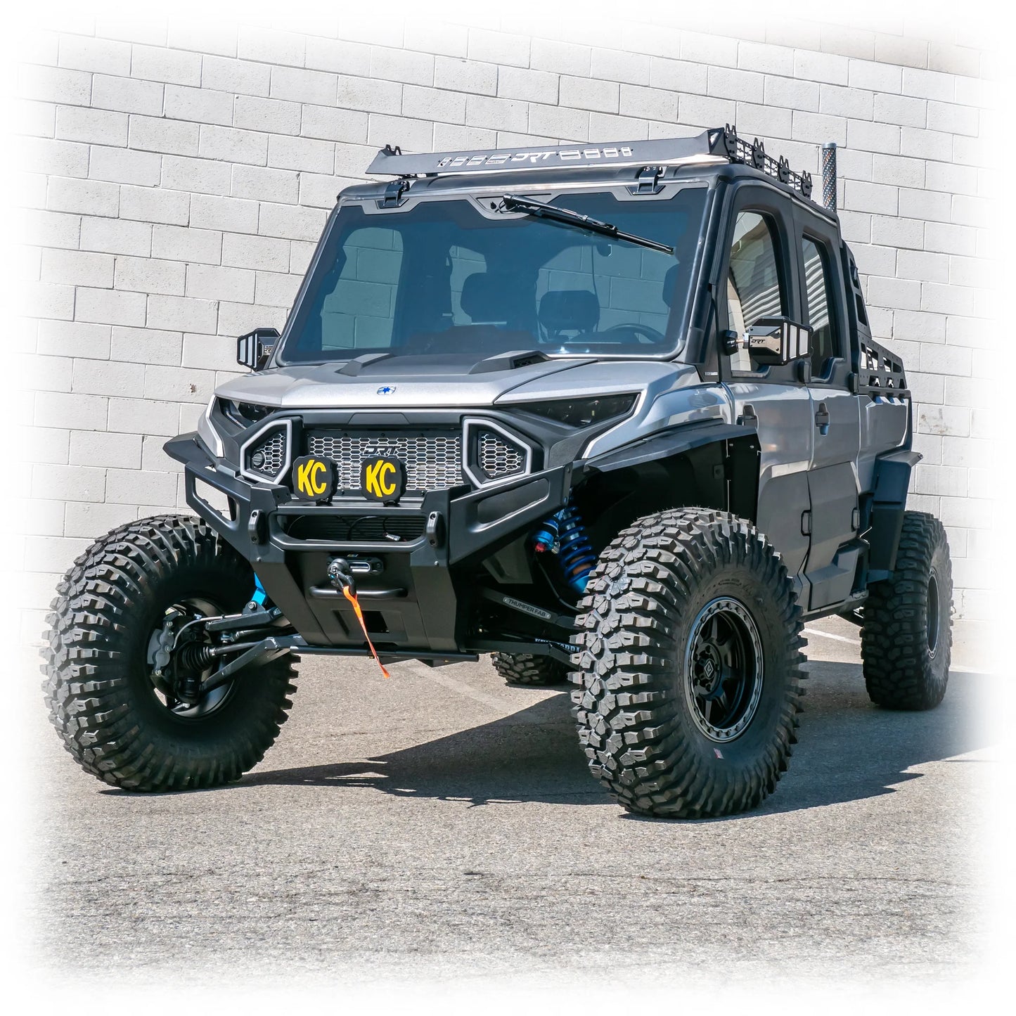 Off-road vehicle with large tires and a rugged design in front of a white brick wall.
