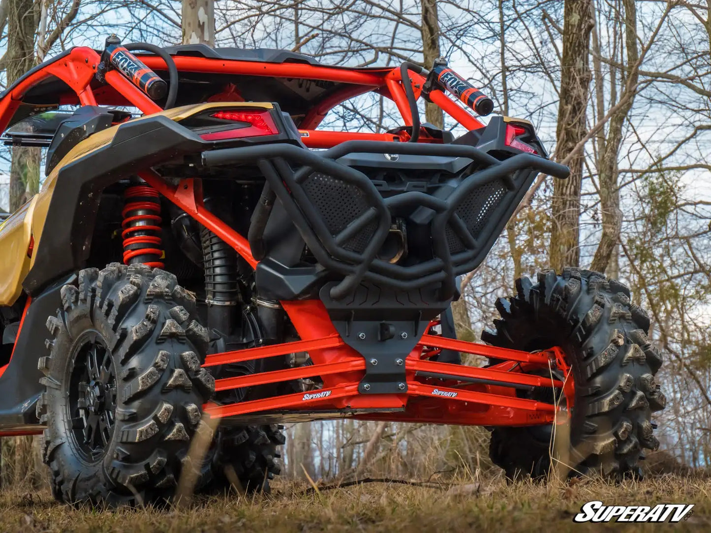 Red and black off-road vehicle with large tires in a forest setting, featuring SuperATV branding.