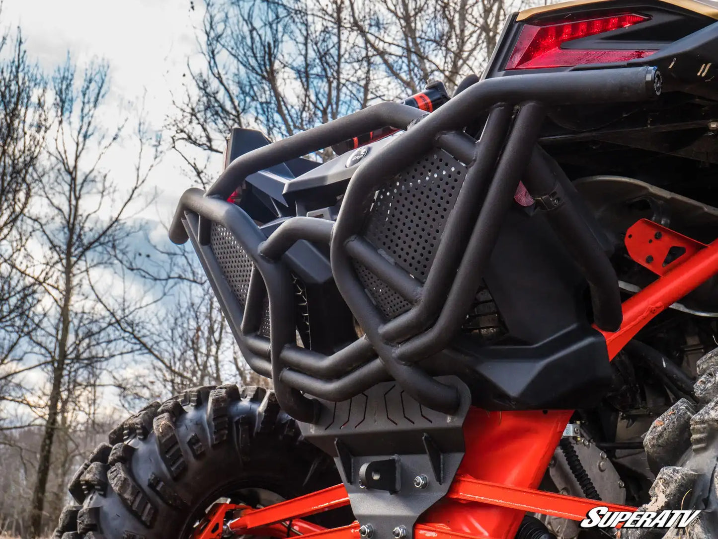 Close-up of a red and black off-road vehicle with a SuperATV bumper in a natural setting.