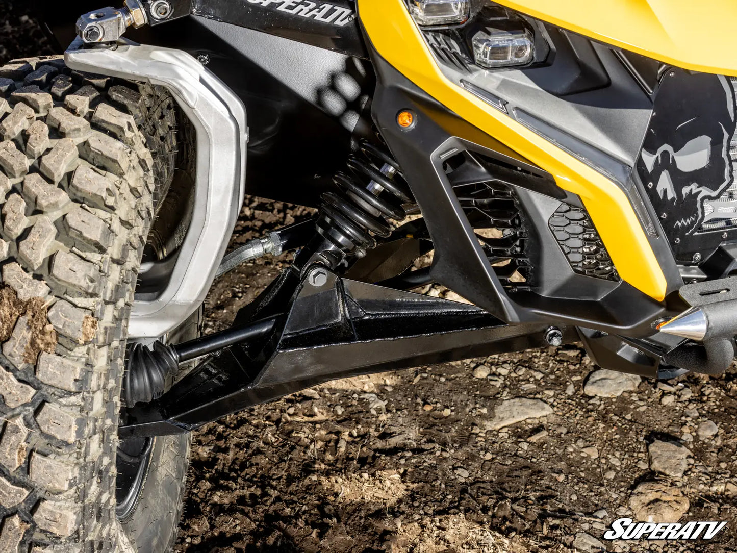 Close-up of a SuperATV vehicle with a focus on the suspension and tire on a dirt surface.