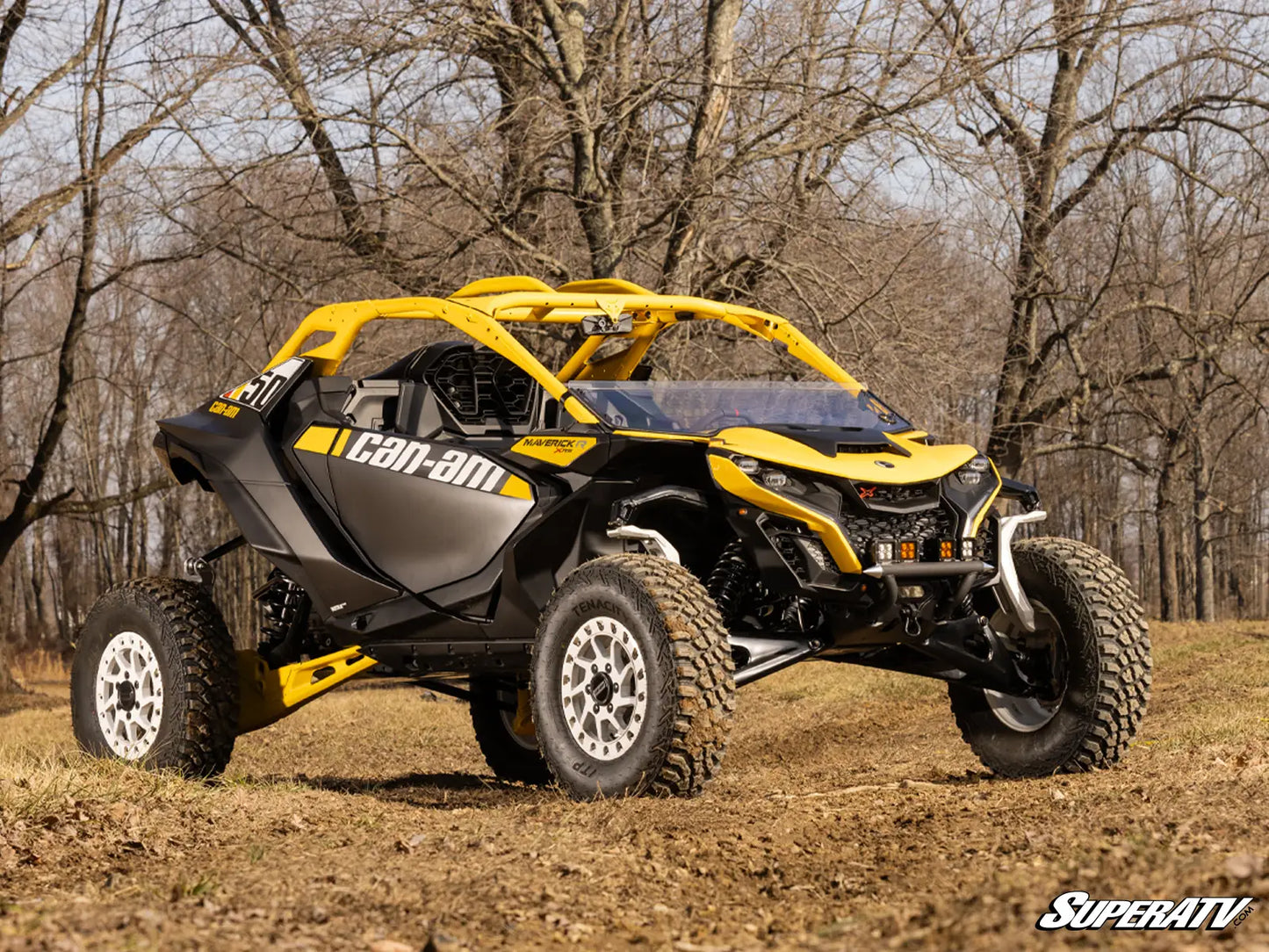 Yellow and black Can-Am vehicle on a dirt path with trees in the background