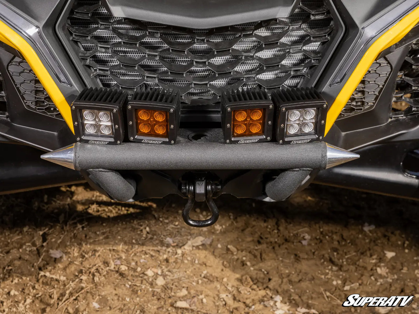 Close-up of a vehicle grille with additional lights on a dirt surface, featuring SuperATV branding.