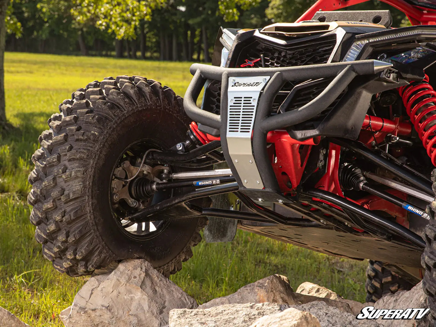 Off-road vehicle with large tires on rocks in a natural setting, featuring SuperATV branding.