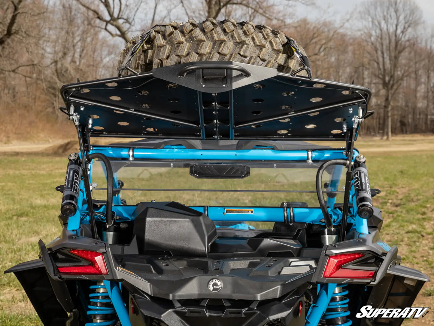 Blue off-road vehicle with large tire and SuperATV logo in a natural setting