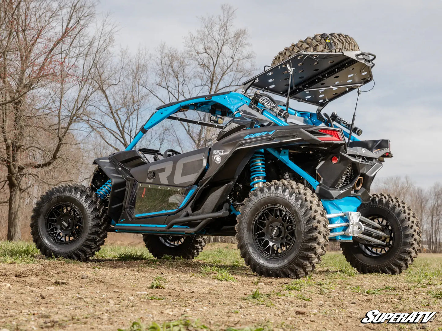 Blue and black SuperATV off-road vehicle on a dirt path with trees in the background