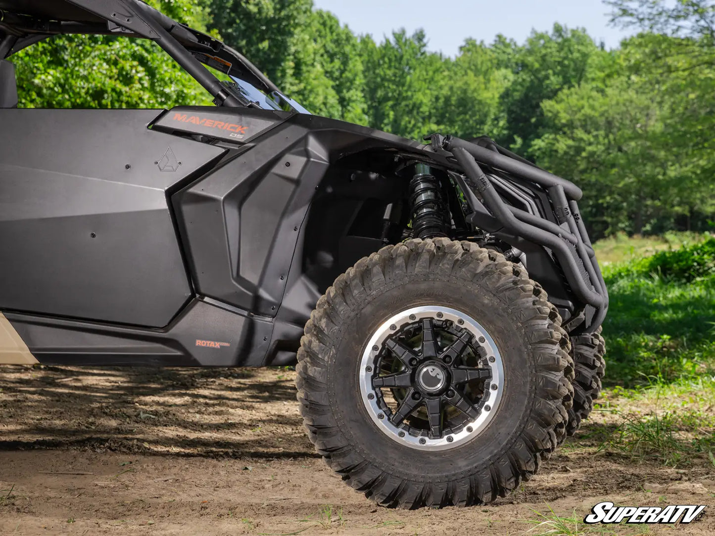 Close-up of a SuperATV vehicle on a dirt path with trees in the background