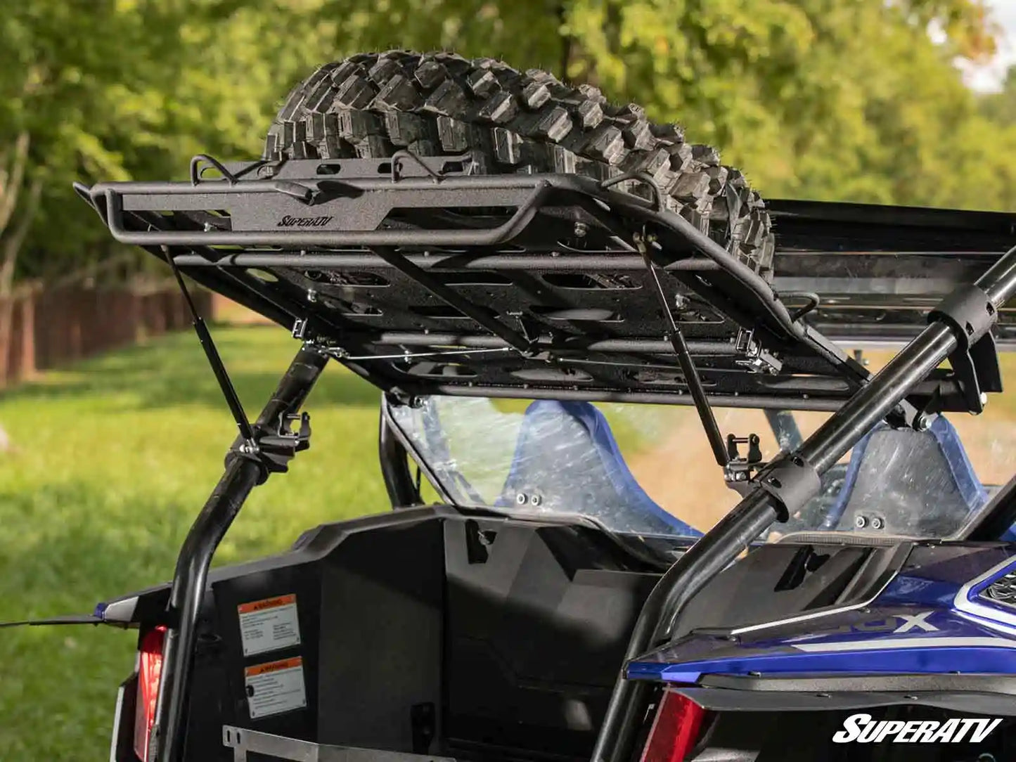Back of a vehicle with a SuperATV rack and tire, outdoors.