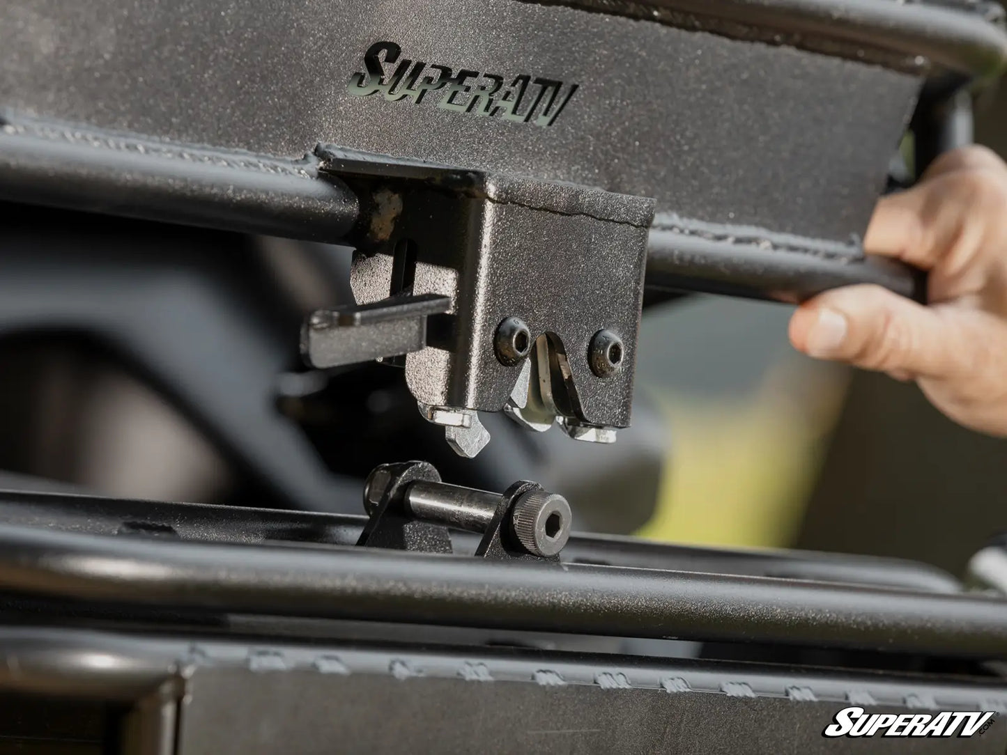 Close-up of a SuperATV product with a hand holding it, against a blurred background.