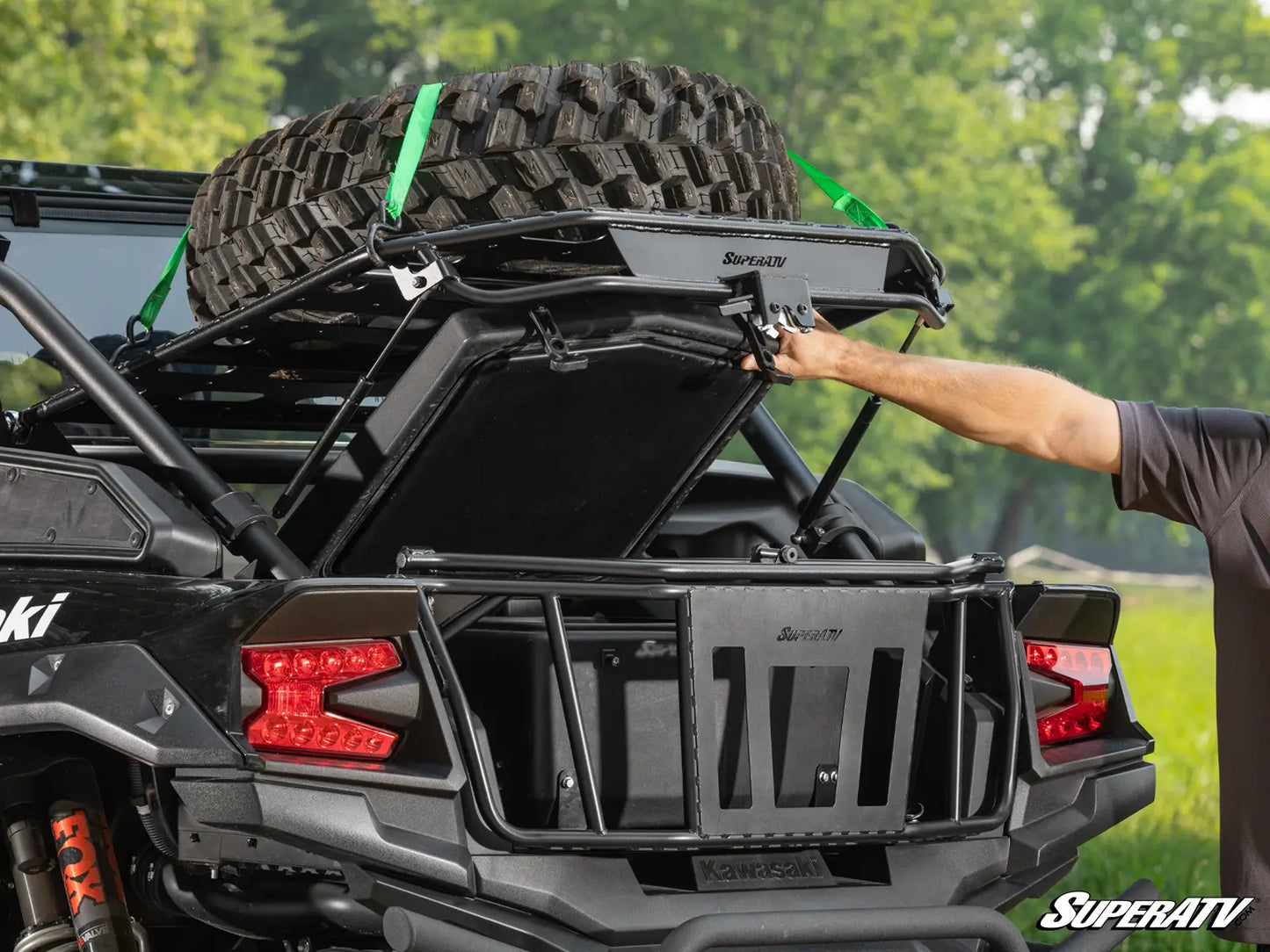Person opening a black SuperATV roof rack on a vehicle with trees in the background