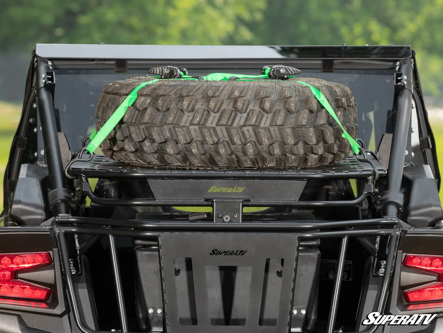 Back of a vehicle with a tire on a SuperATV rack against a blurred green background