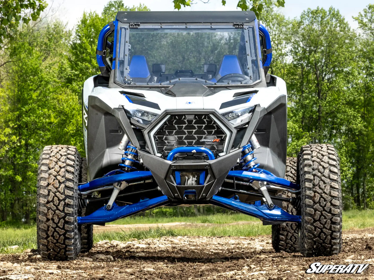 Off-road vehicle with blue accents on a dirt path surrounded by trees, featuring the SuperATV logo.