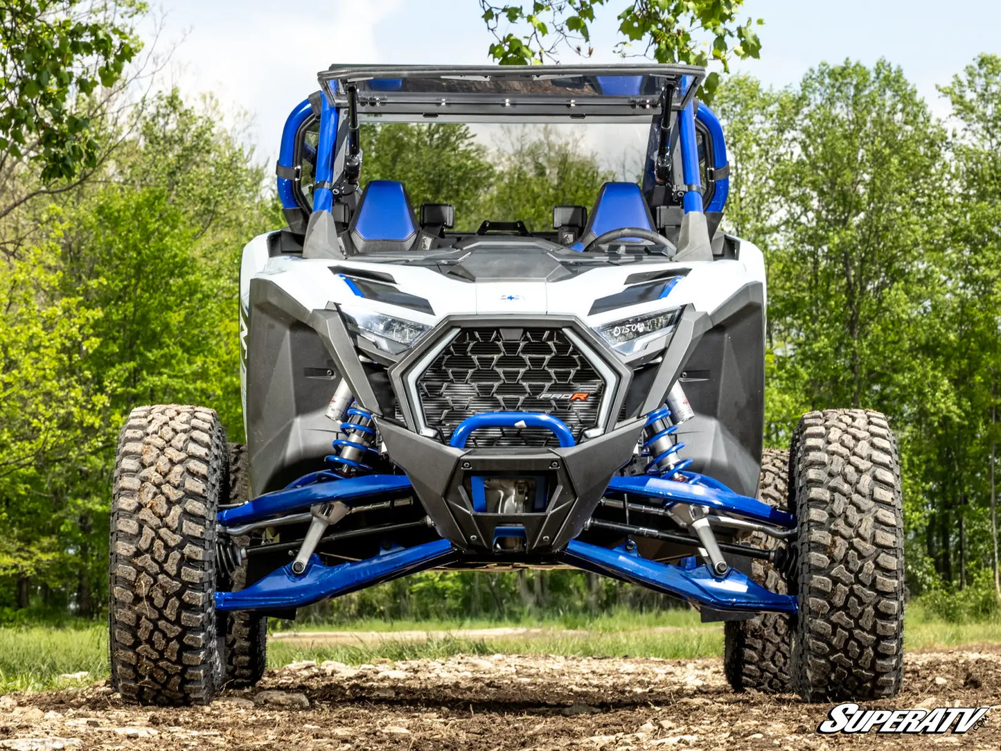 White and blue off-road vehicle on a dirt path with trees in the background