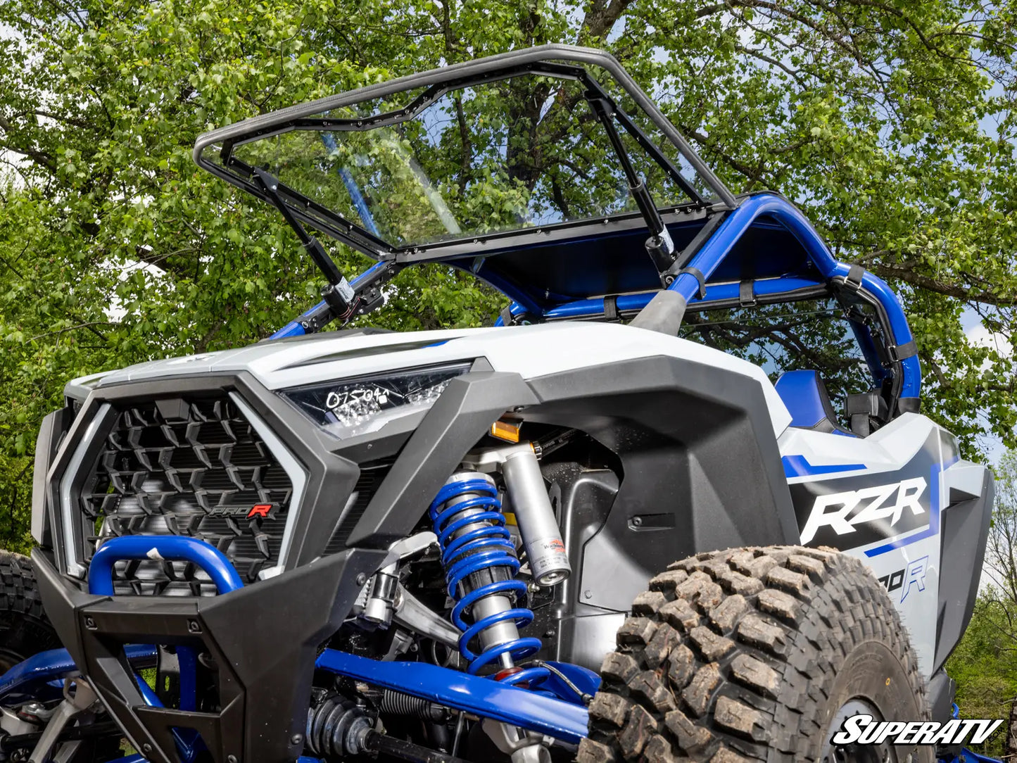 Side view of a Polaris RZR with SuperATV branding, surrounded by greenery.