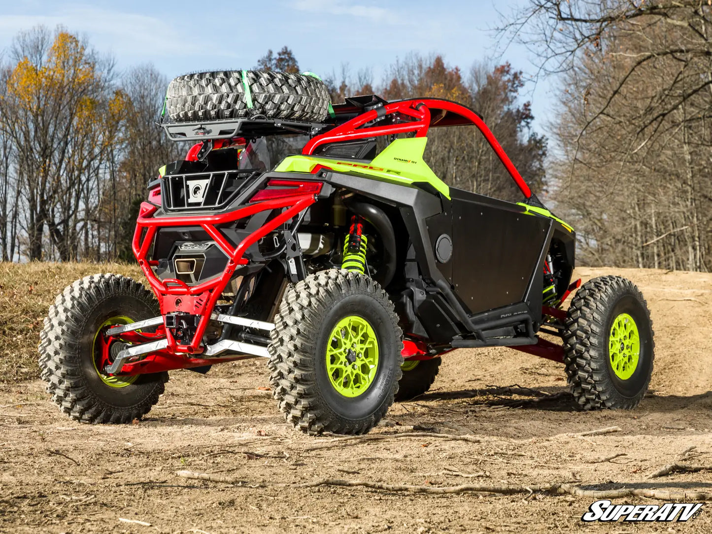 Off-road vehicle with large tires on a dirt path, surrounded by trees with autumn foliage.