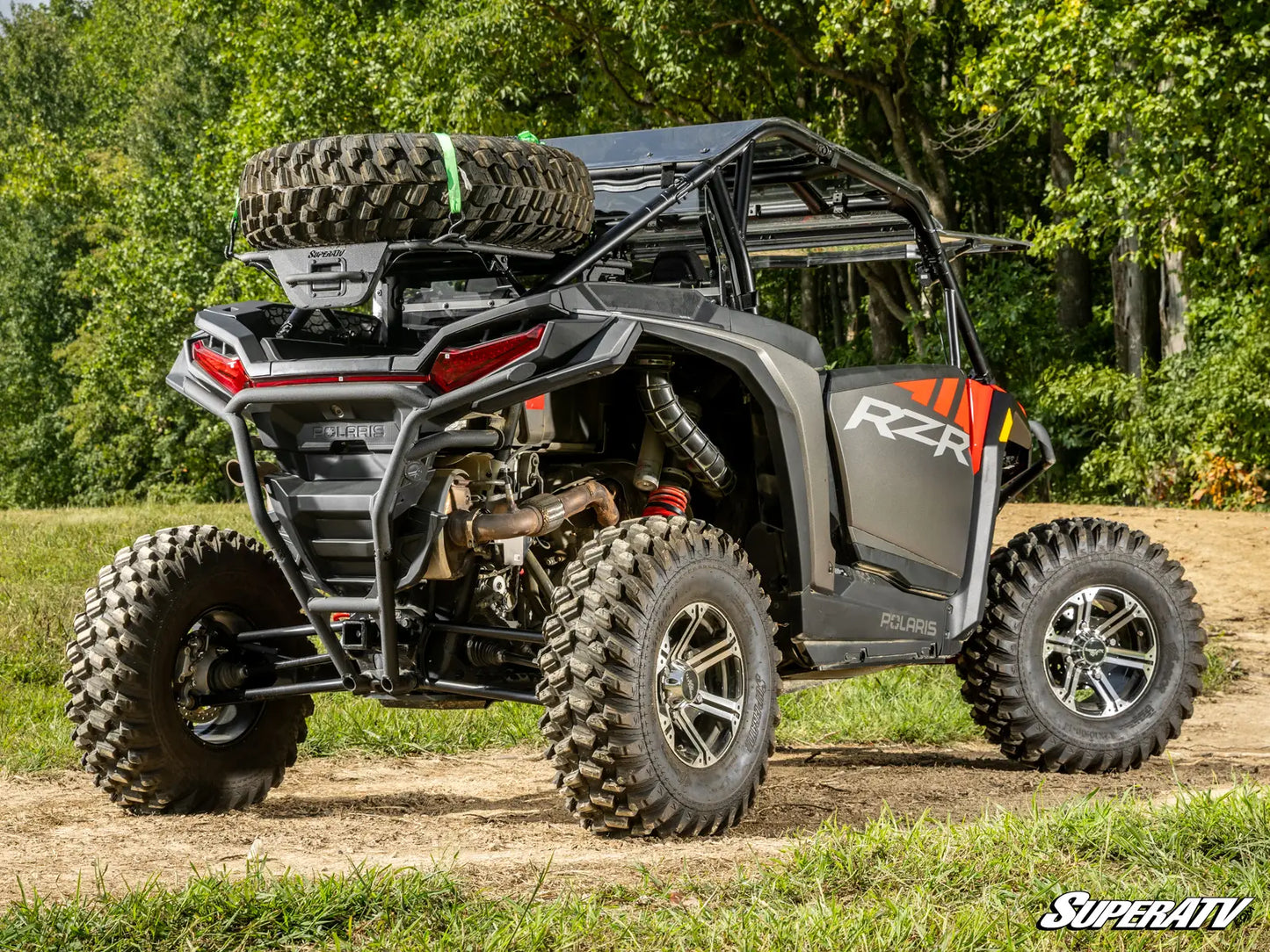 Off-road vehicle with large tires on a dirt path surrounded by trees