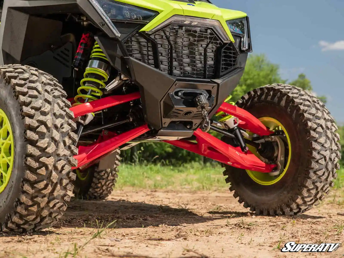 Close-up of a SuperATV vehicle on a dirt road with greenery in the background