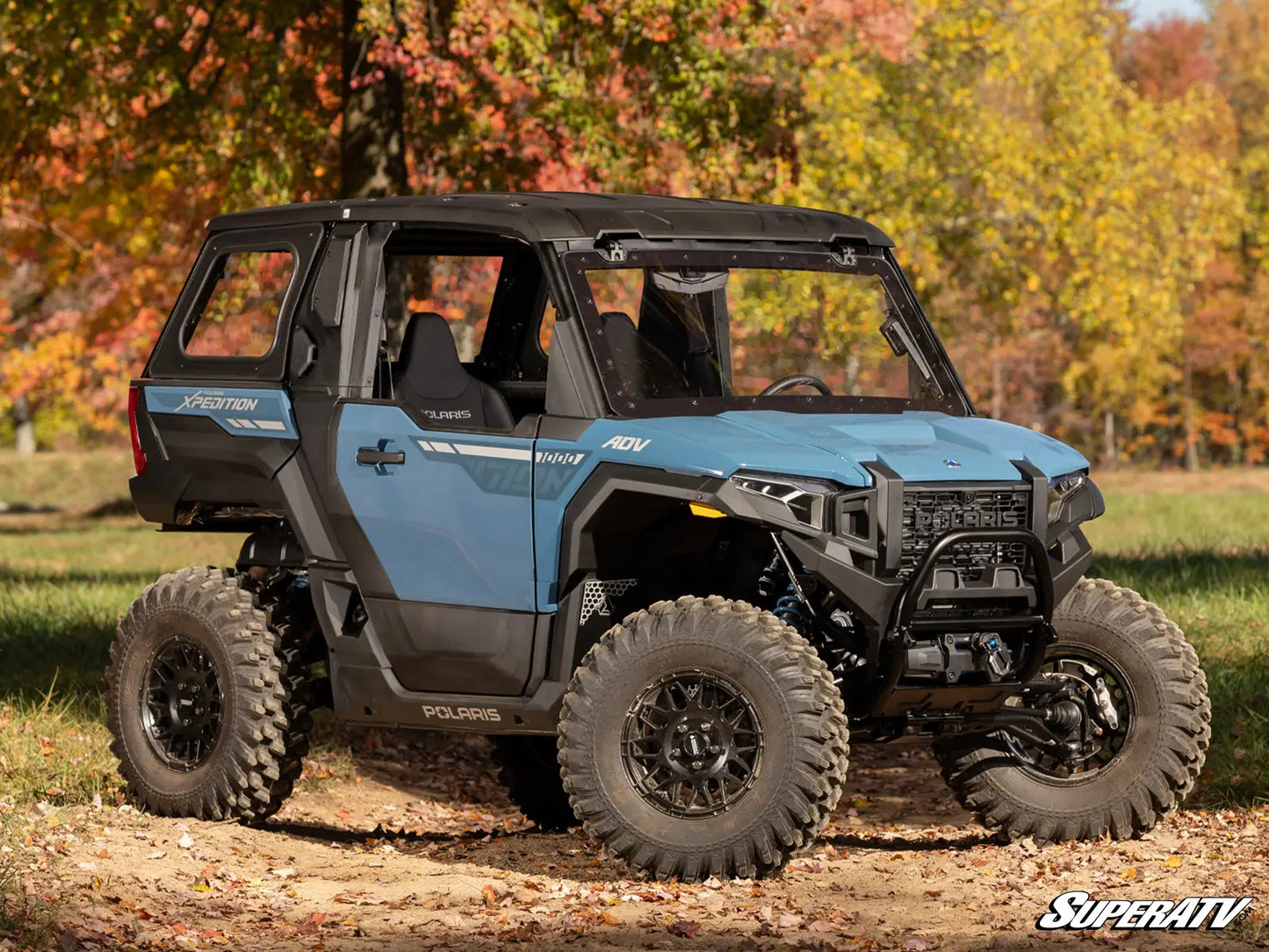 Blue Polaris SuperATV vehicle on a dirt path with autumn trees in the background