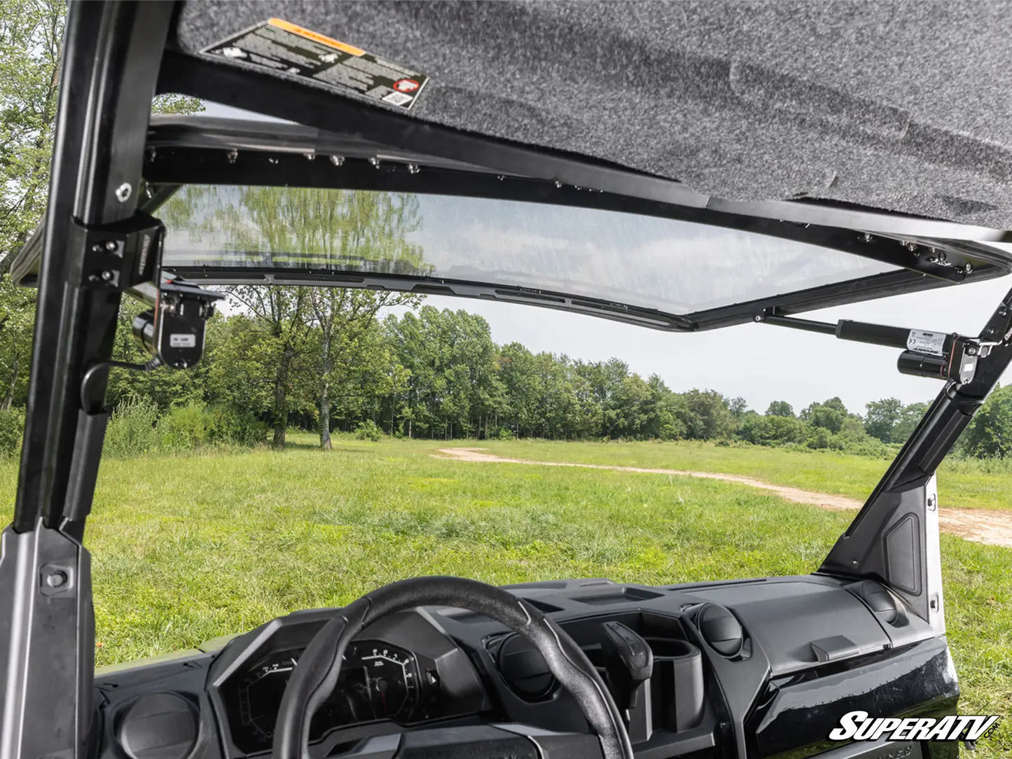 Interior of a SuperATV vehicle with open roof showing a grassy field and trees outside.