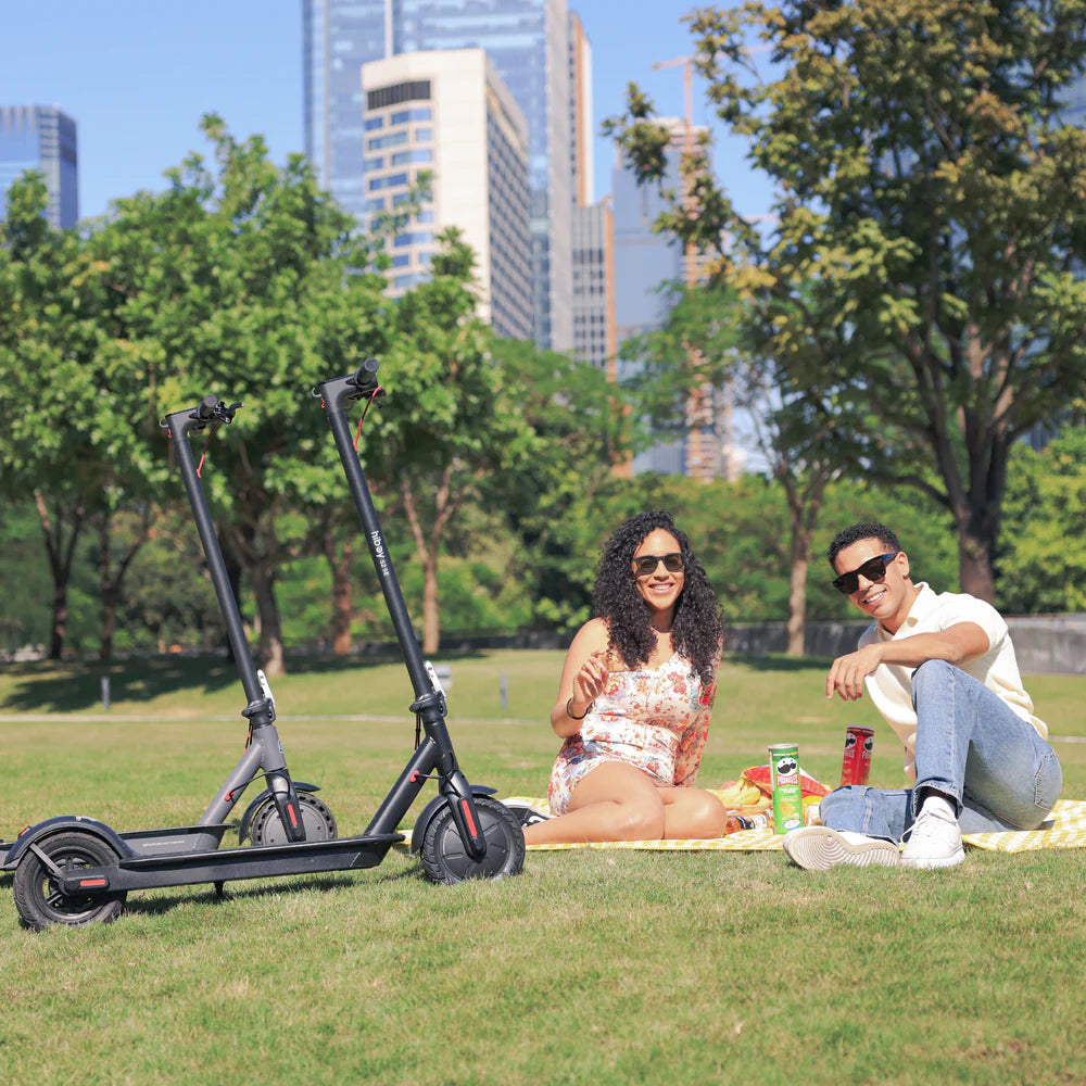 Two electric scooters on a grassy area with a city skyline in the background