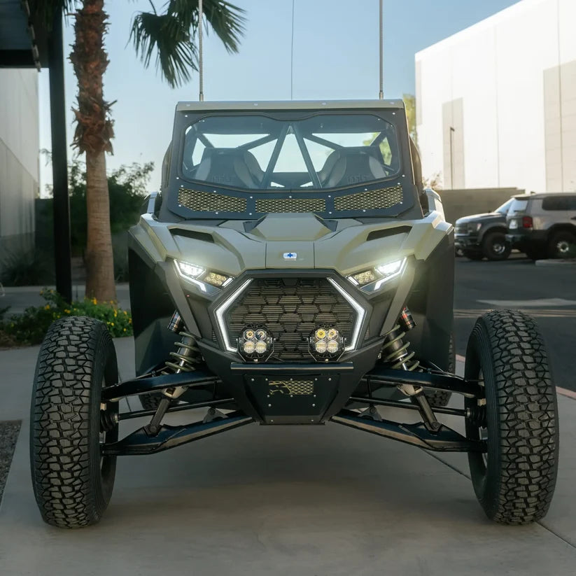 Front view of a Polaris RZR off-road side-by-side vehicle parked on a concrete driveway with palm trees and a building in the background.