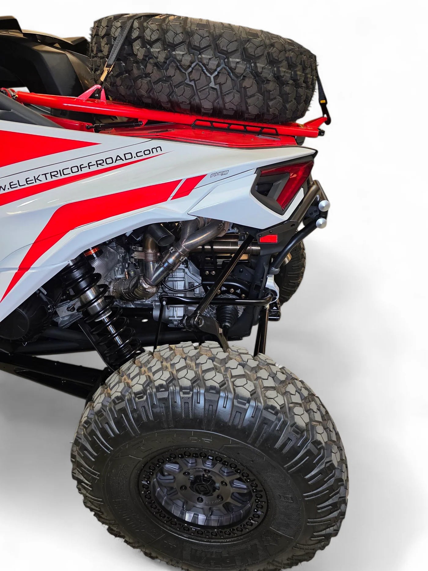 Close-up of a red and white off-road vehicle with large black tires on a white background.