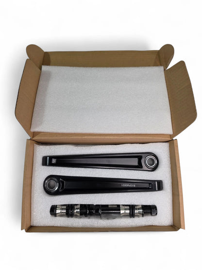 Three black metal components in a cardboard box with styrofoam padding.