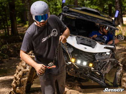 Person with SuperATV gear standing next to an off-road vehicle in a forest setting