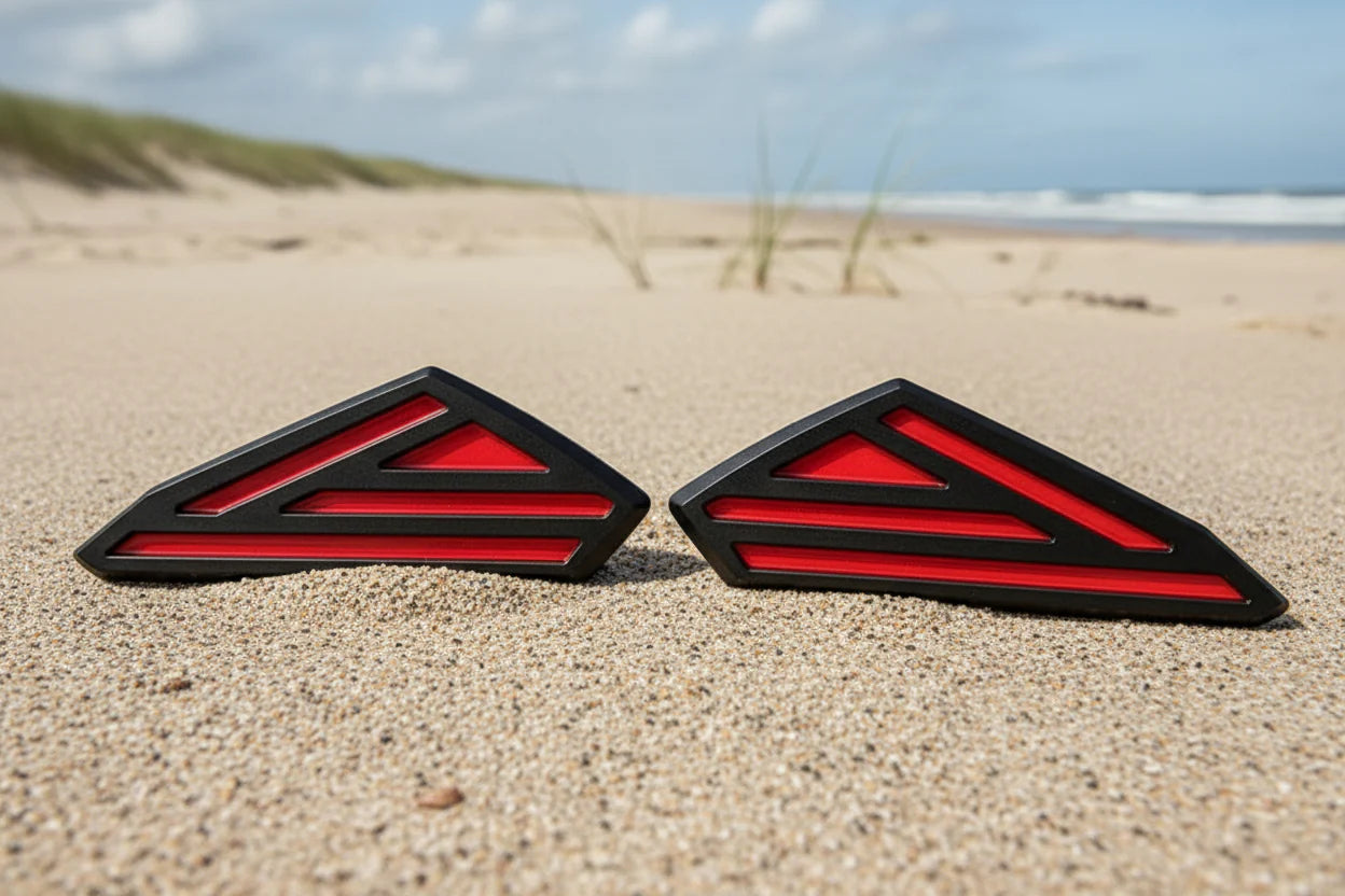Two red and black triangular objects on a sandy beach with grass and water in the background.