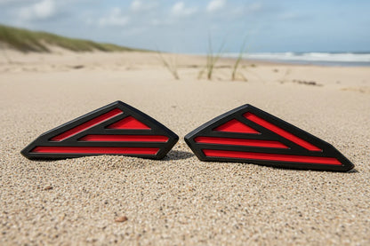 Two red and black triangular objects on a sandy beach with grass and water in the background.