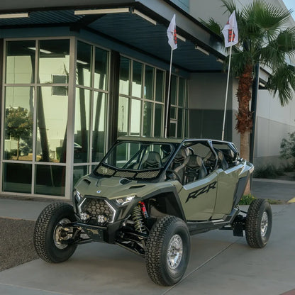 Green off-road vehicle parked in front of a building with large windows and palm trees.