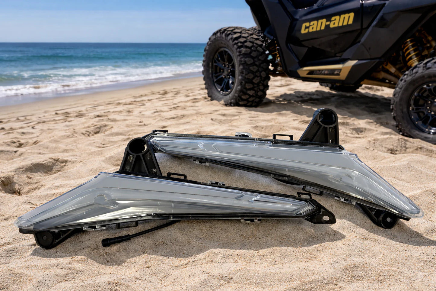 Can-Am vehicle parts on a sandy beach with ocean in the background