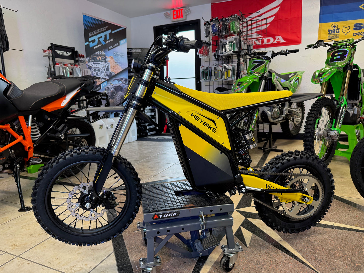 Yellow and black dirt bike on display in a showroom with various motorcycles in the background.