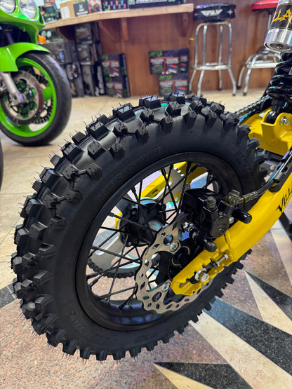 Close-up of a dirt bike wheel with knobby tire on a patterned floor.