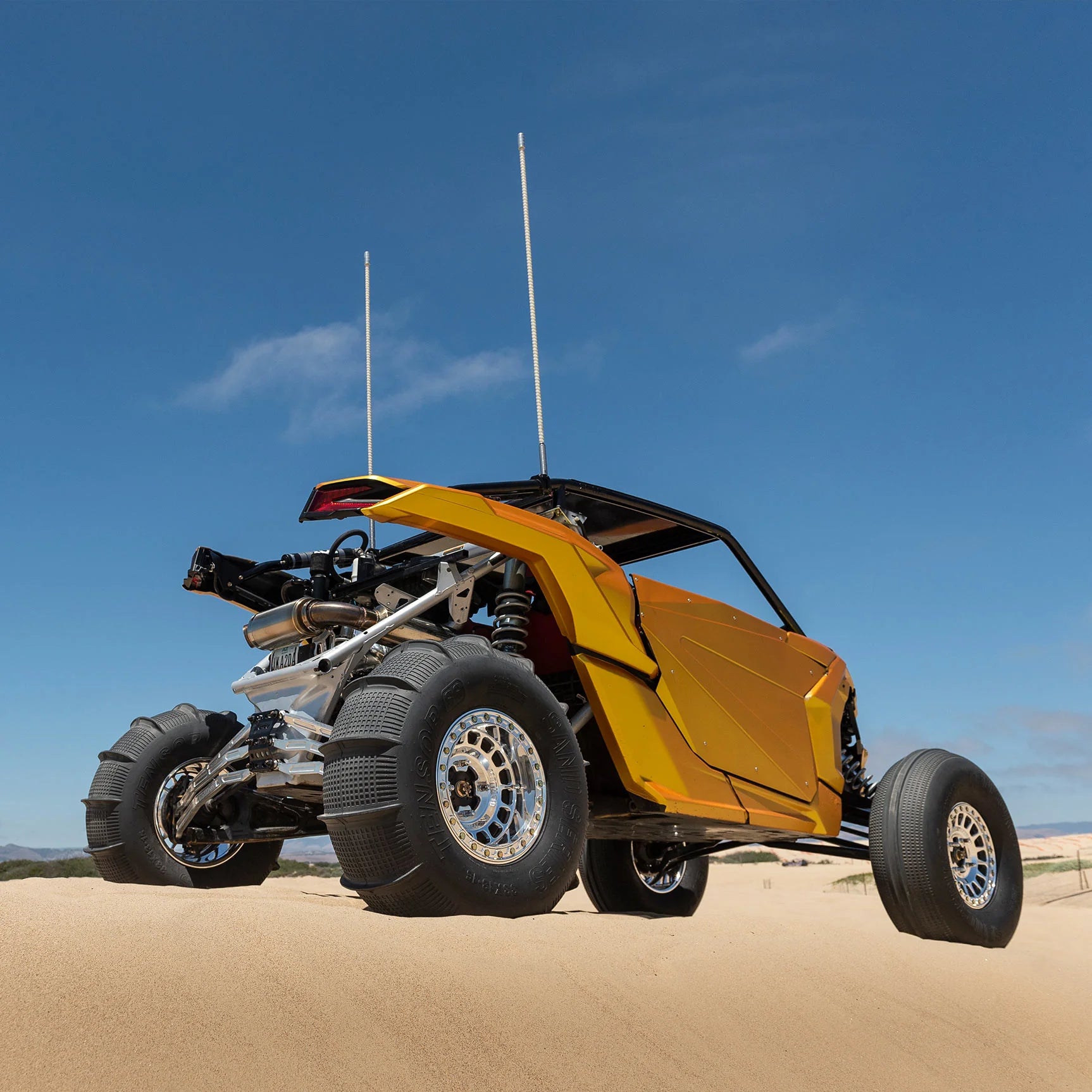Yellow off-road vehicle on a sandy terrain with a clear blue sky.