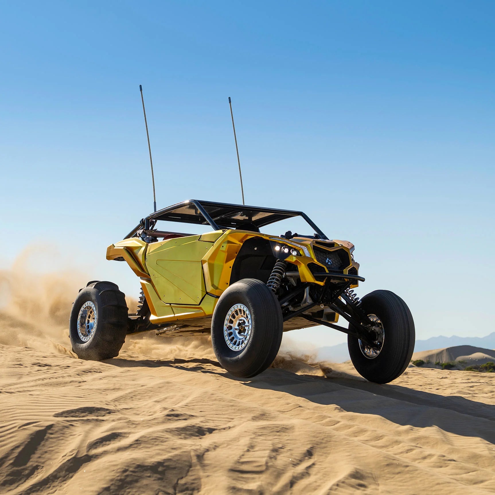 Yellow off-road vehicle driving on sand with a clear blue sky