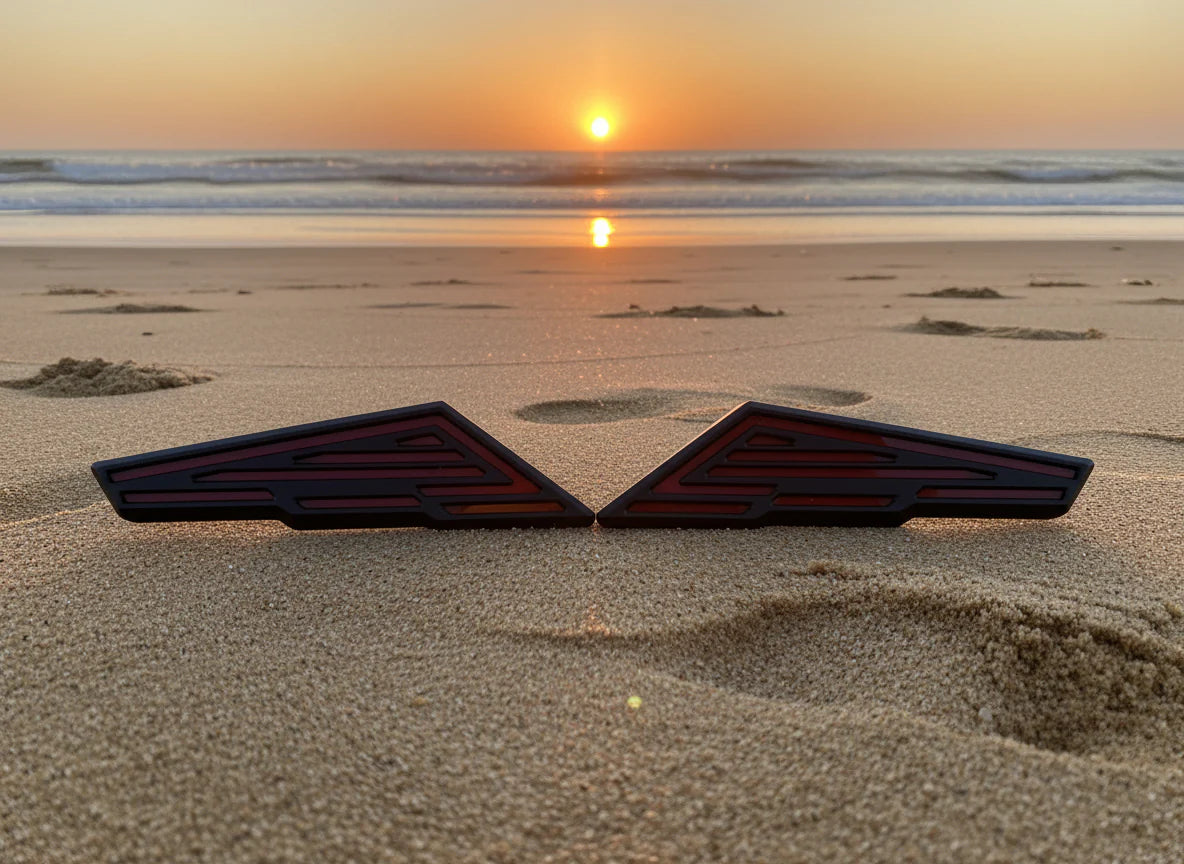 Two black triangular objects on a sandy beach with a sunset in the background.