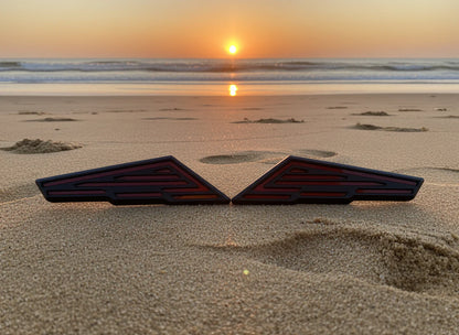 Two black triangular objects on a sandy beach with a sunset in the background.