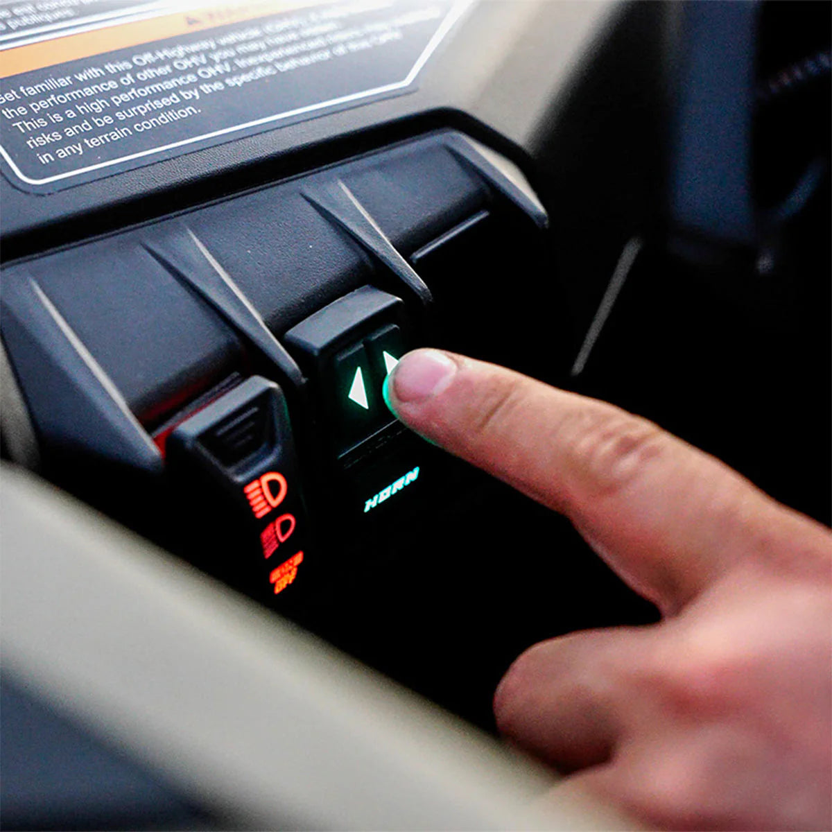 Hand pressing a button on a vehicle's control panel with illuminated icons.