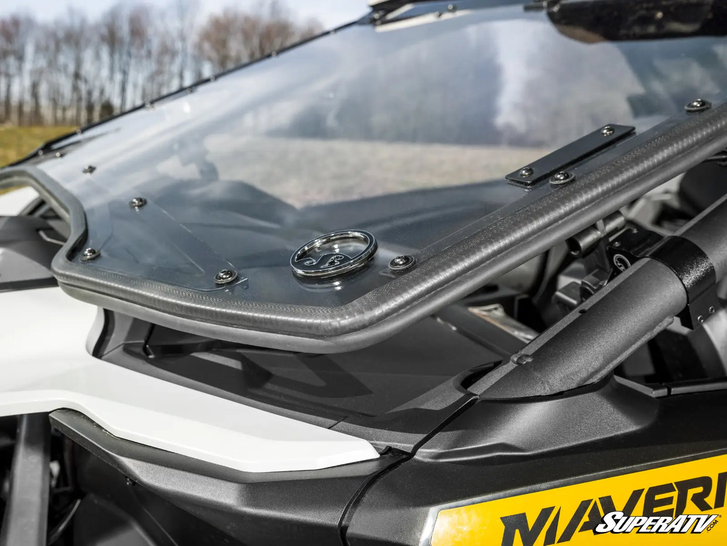 Close-up of a motorcycle windshield with a brand logo on a blurred natural background