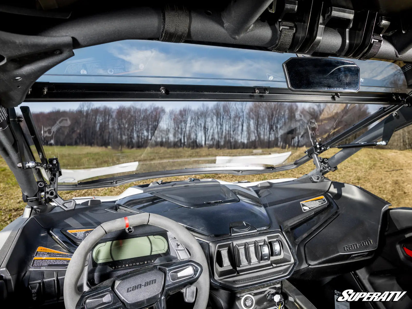 Close-up of a SuperATV vehicle interior with dashboard and steering wheel, showing a clear sky and trees in the background.