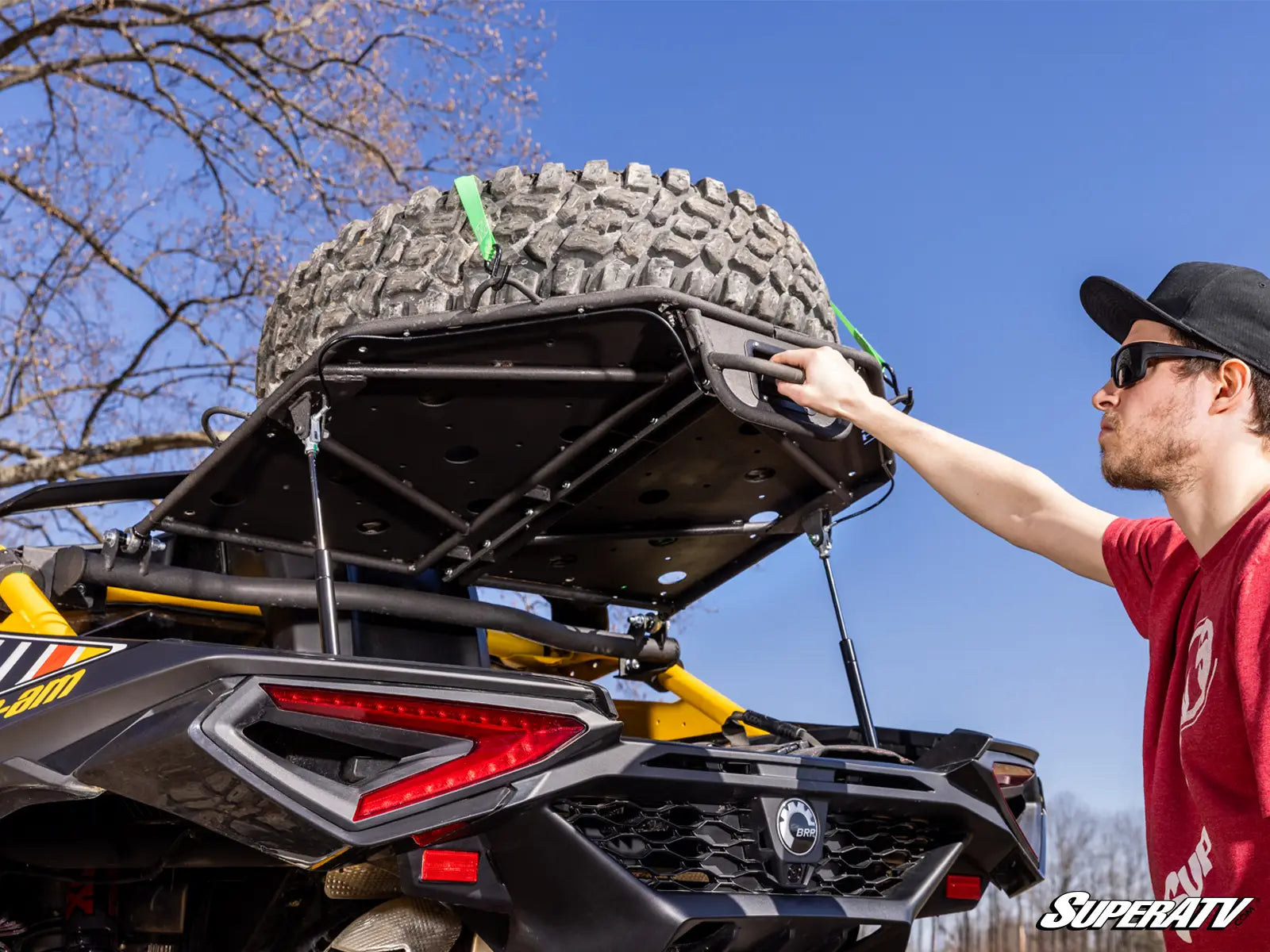 Person attaching a tire to a SuperATV vehicle with a clear blue sky background