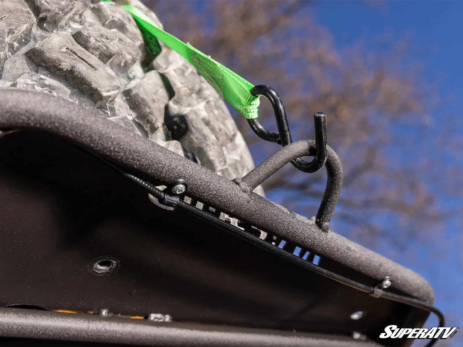 Close-up of a roof rack system on an ATV with a green strap against a blue sky and tree background.