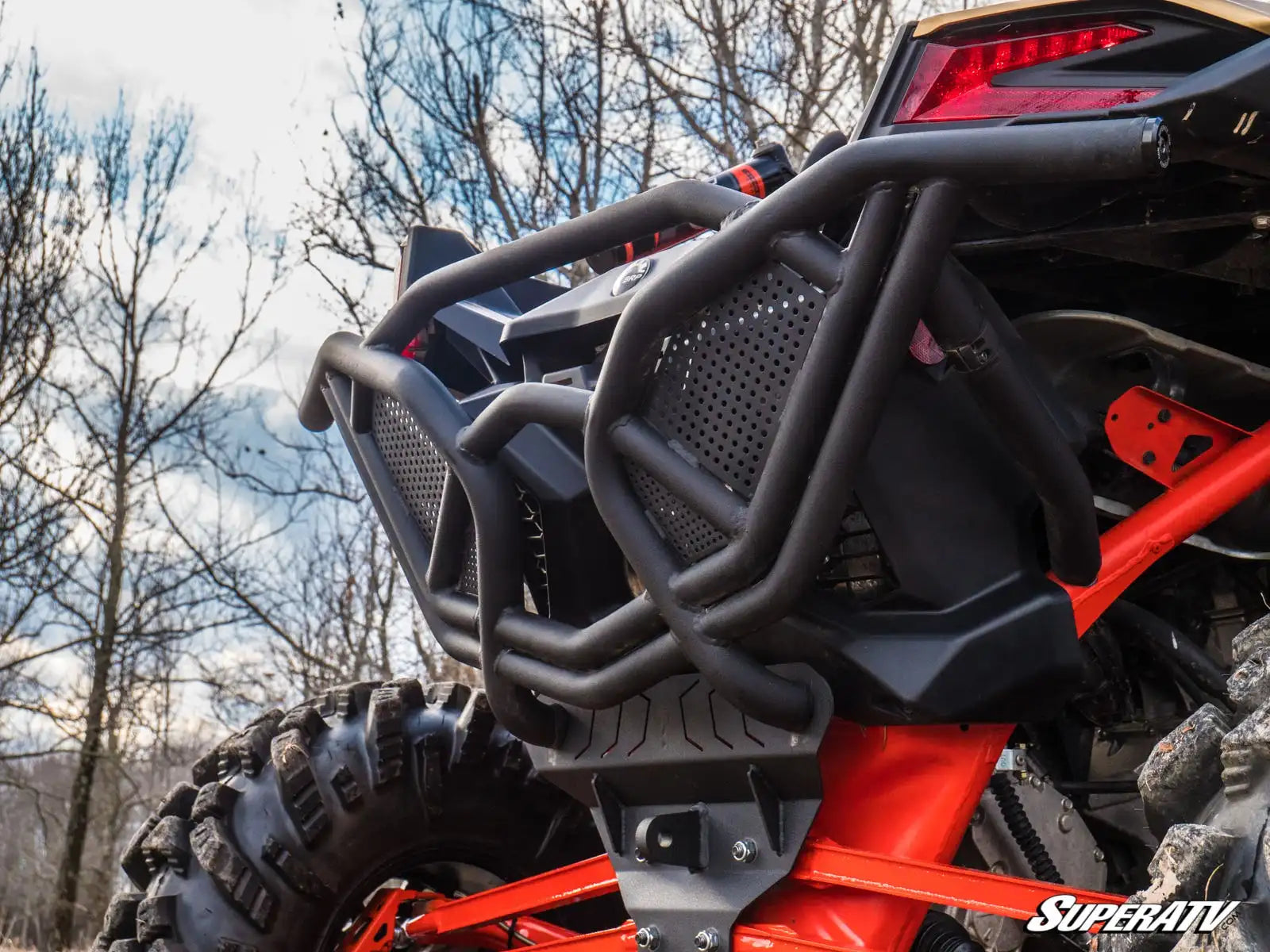 Close-up of a red and black off-road vehicle with a SuperATV bumper in a natural setting.