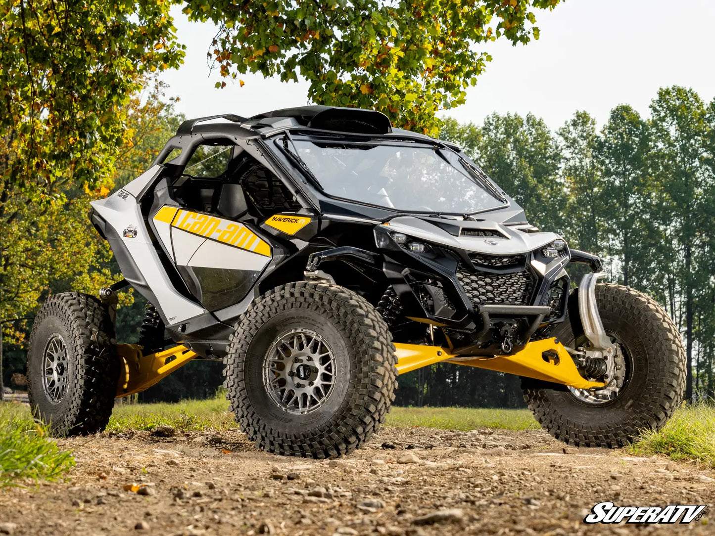 Yellow and black SuperATV off-road vehicle on a dirt path with trees in the background