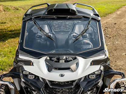 Front view of a Can-Am vehicle with a clear windshield and wipers on a grassy and dirt path background.