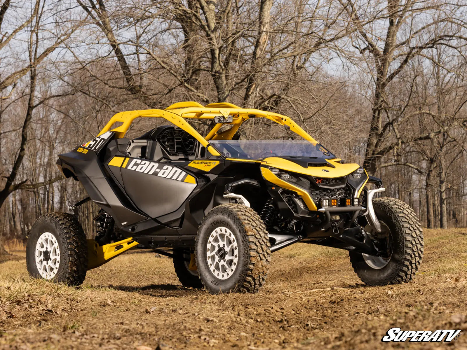Yellow and black Can-Am vehicle on a dirt path with trees in the background