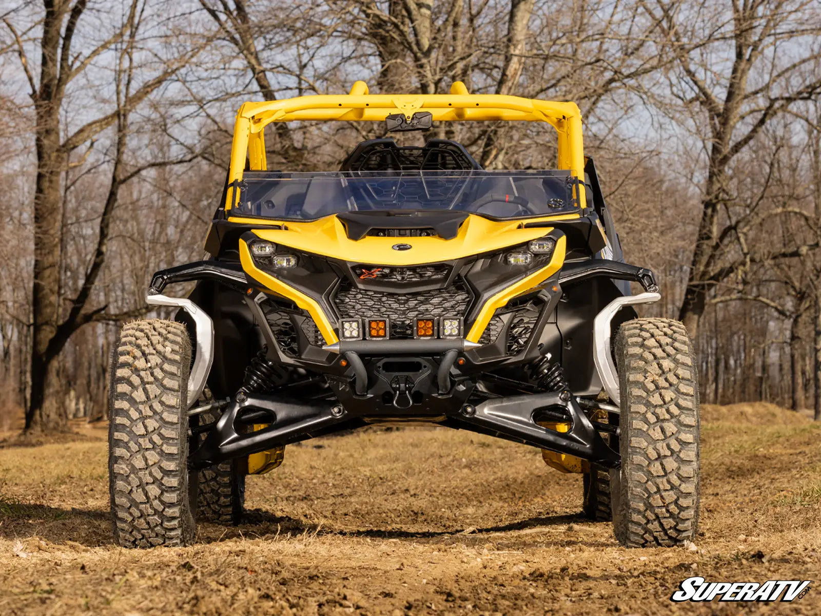 Yellow and black SuperATV vehicle on a dirt path with trees in the background