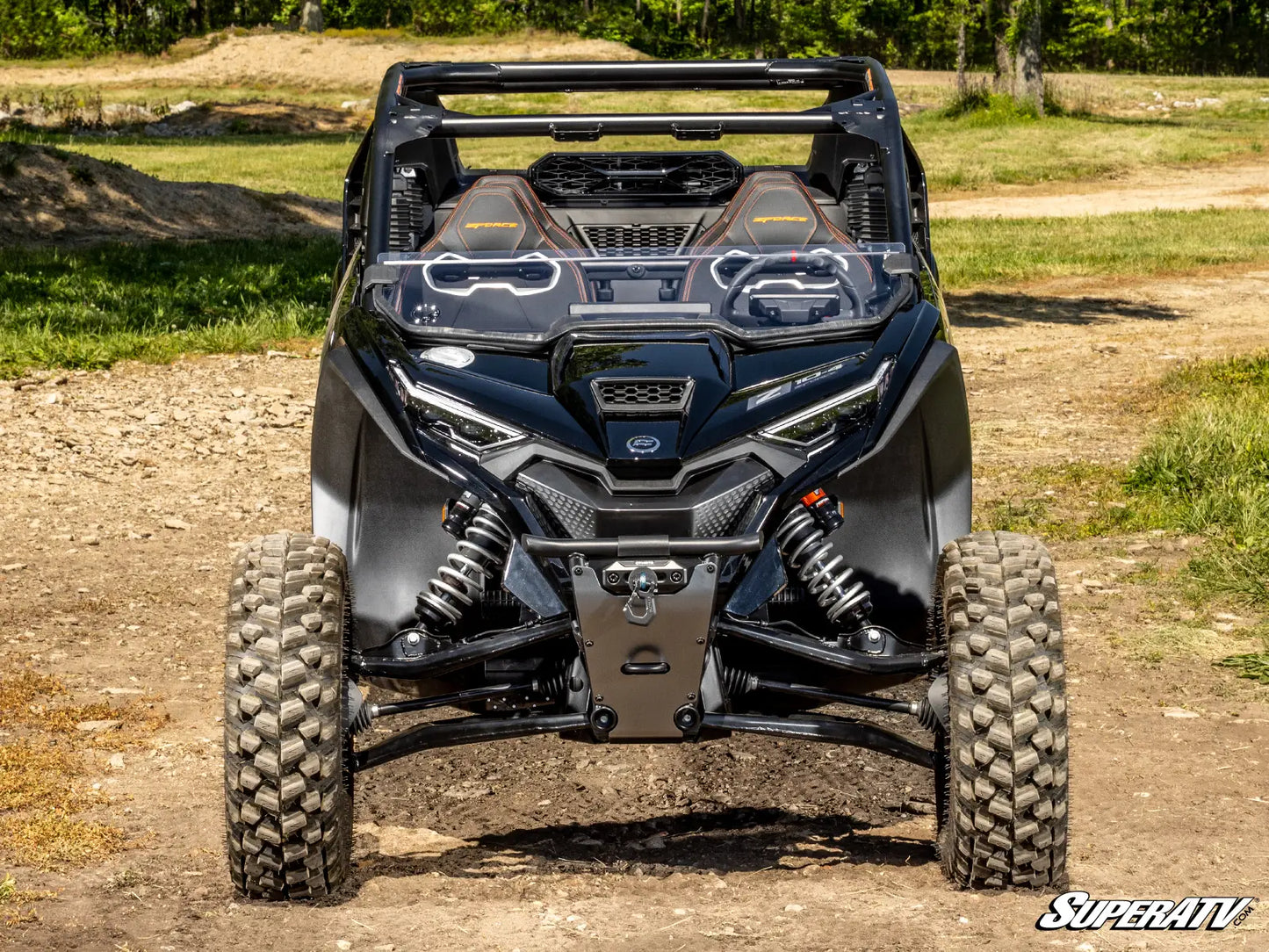 Front view of a black SuperATV vehicle on a dirt road with grass and trees in the background.