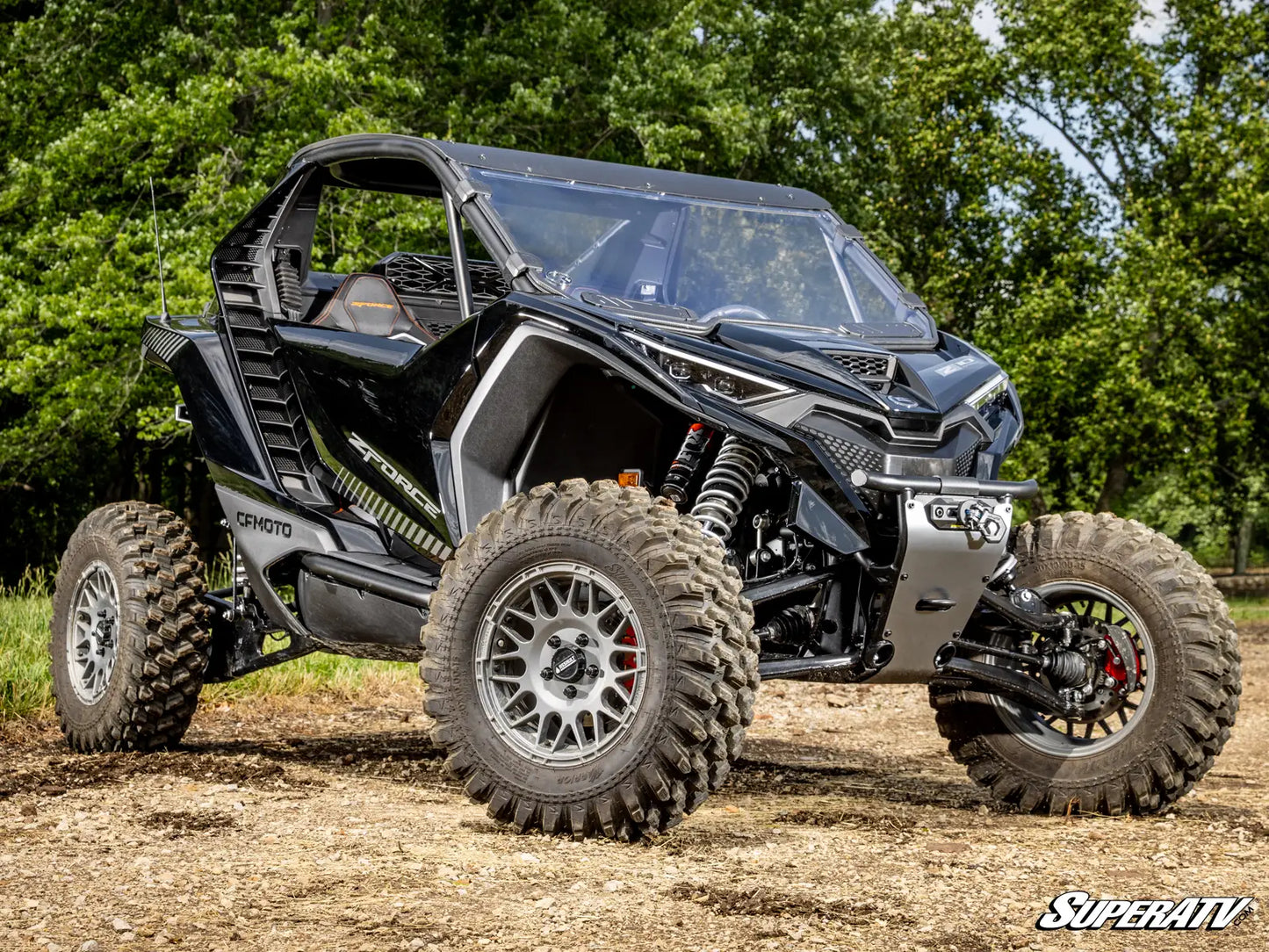 Black SuperATV off-road vehicle on a dirt path with trees in the background